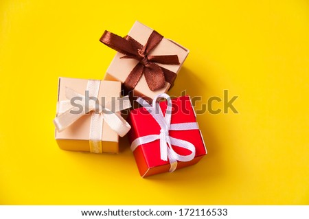 Three wrapped colorful gift boxes with colorful satin ribbons and bows on yellow background in studio, Focus on a bow