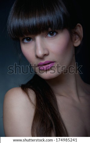 Mysterious pretty young brunette woman model with hazel eyes, straight fringe, natural makeup, emphasis on pink lips, looking at camera. On black background. Cold skin type