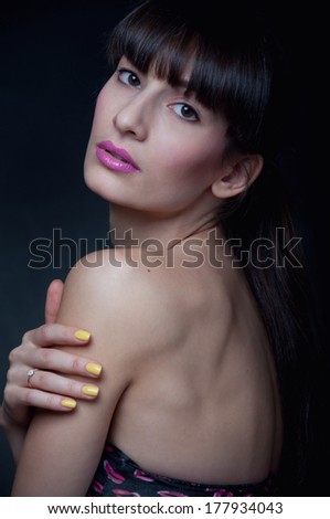 Studio portrait of young pretty woman model with bright yellow nails, wearing pink lipstick and black top with pink lips pattern on it. Looking at camera. Black background