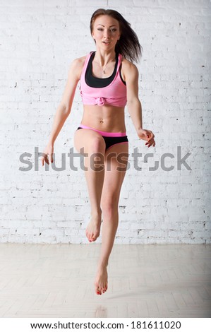 Beautiful strong sports woman wearing black pink tee top, shirts, running towards the camera, jumping up. Against brick wall