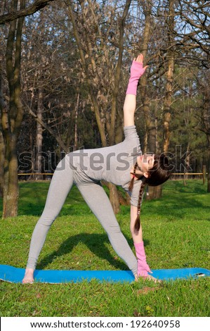 Beautiful woman practicing yoga asanas outdoors on a warm spring day in a park, keeping balance while doing a warrior pose