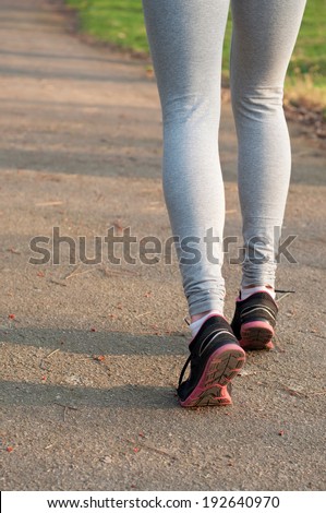Female runner feet running on the road outdoors at nature. Closeup, main focus on the shoe. On a bright sunny spring day