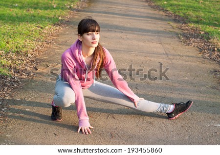 Pretty sporty brunette woman athlete stretching her legs after a run over the park. On a bright sunny day, at sunset