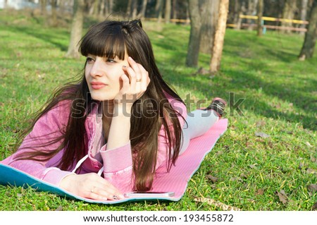 Happy brunette woman lying on the grass on a mat and enjoying the bright sunny day, dreaming about something