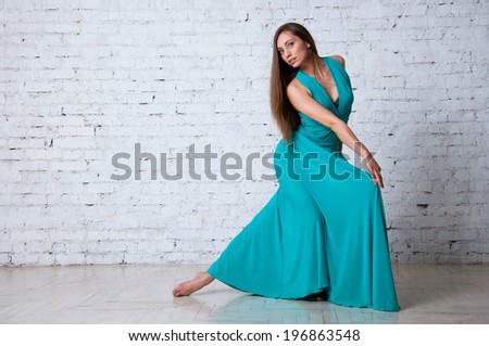 Pretty woman dancer wearing beautiful turquoise dress, dancing flamenco in studio over brick wall background