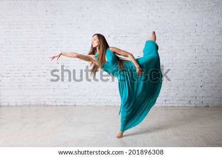 Pretty woman dancer doing pirouette, posing, dancing, jumping in a studio, standing on tiptoes, long blue turquoise long dress getting into drapes, hair flying in the air. Over brick wall background