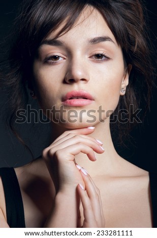 Young and beautiful brunette woman with natural makeup looking at camera, her lips half open. Over dark grey background