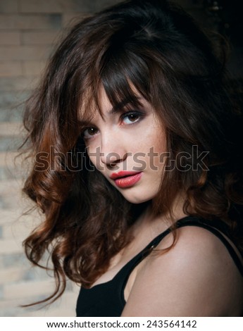Pretty young brunette woman with curly hair looking at camera. Main focus on face