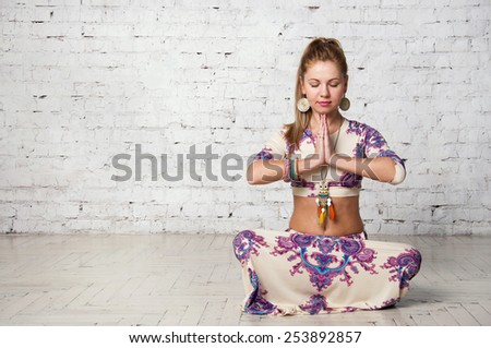 Pretty young blond female yoga sitting in a lotus pose, meditating in a studio. Against brick wall background, copy space