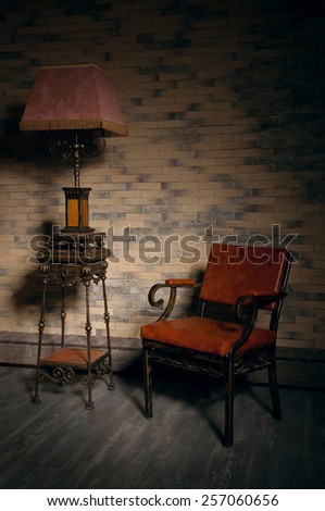Beautiful ornate stand lantern standing near a leather armchair in empty room. Nice play of shadows on the wall. Copy space