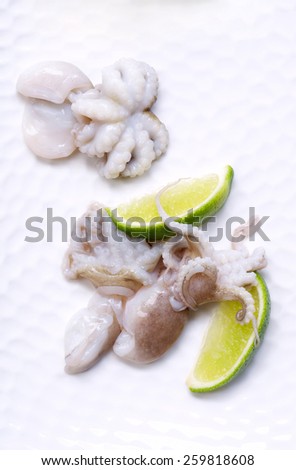 Fresh baby octopus being pickled with lime slices on a white plate. On the table, still life, copy space