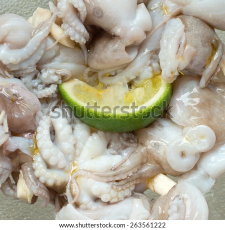 Fresh baby octopus being pickled with lime slice, garlic and olive oil in a glass bowl before cooking. On the table, still life, copy space