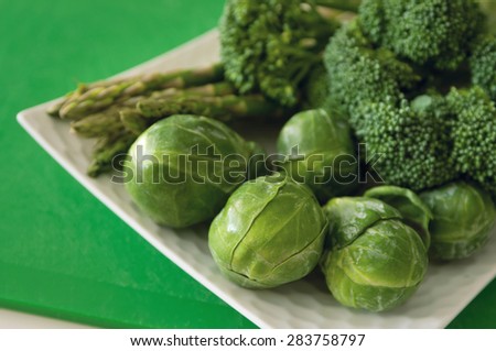 Healthy fresh vegetables broccoli, brussels sprout and asparagus bunch on a white plate against green background.