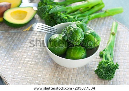 Fresh ripe juicy and delicious vegetables brocolli, brussels sprouts, bunch of asparagus, avocado cut in halves, herbs and spices on wickered mat on table ready to be cooked, can be used as background