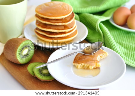Delicious golden pancakes cooked on dry pan and served for breakfast with honey and kiwi fruit on a wooden board, one pancake half eaten. Still life, copy space