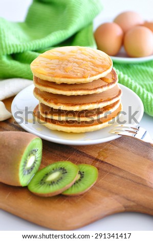 Delicious golden pancakes cooked on dry pan and served for breakfast with honey and kiwi fruit on a wooden board. Still life, copy space