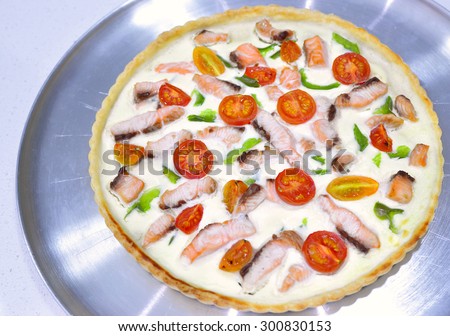 Delicious variation for quiche pie and pizza - whole pie with thickened cream cottage cheese, salmon, green capsicum cherry tomatoes cut in halves, on aluminium tray plate. Selective focus, top view