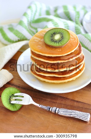 Delicious golden pancakes cooked on dry pan and served for breakfast with honey and kiwi fruit on a wooden board. Still life, copy space