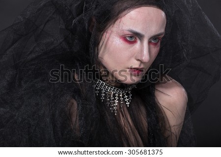 Art picture of a girl with stylish make-up in shades of red , covered with fabric - tulle on a black background