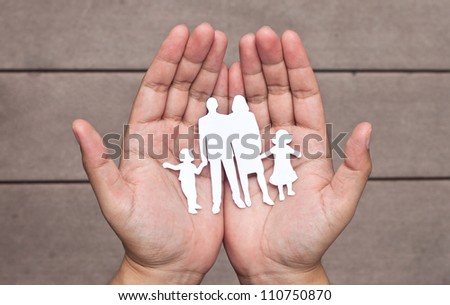 Paper family in hands on brown wood background