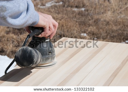 Sanding Wooden Table - A carpenter uses a hand held random orbit power sander to smooth a hand crafted table top.