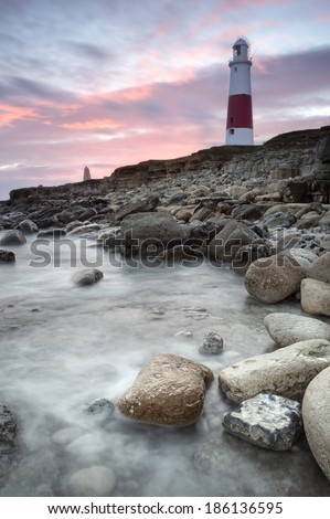 Portland Bill Lighthouse stands sentinel on the rugged south England coast as sun sets; its light warding boats from the perilous waters and rocks.
