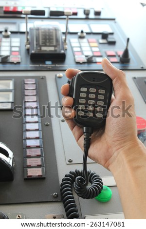 Hand holding two way radio receiver on bridge of ship