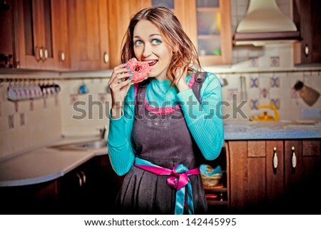Beautiful woman in a kitchen bitten donut
