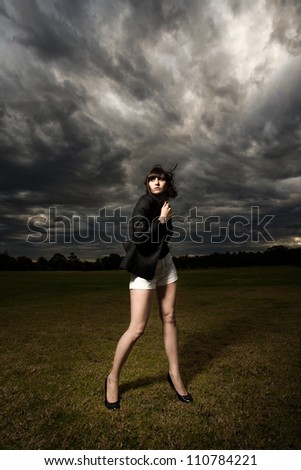 Young caucasian woman with fringe/bangs white shorts and suite jacket in a park with stormy background