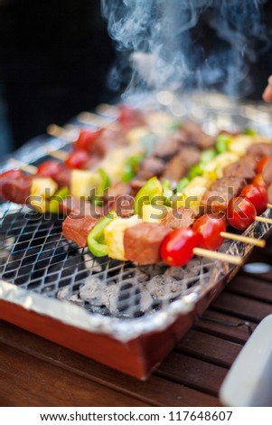 Thai style BBQ beef and vegetables on skewer grilling on a plate in outdoor cooking area.
