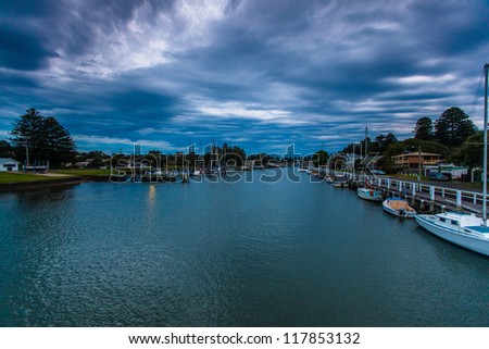 View from evening footbridge walkway across Moyne River in Port Fairy, VIC. Calm water with dramatic cloud overhead.