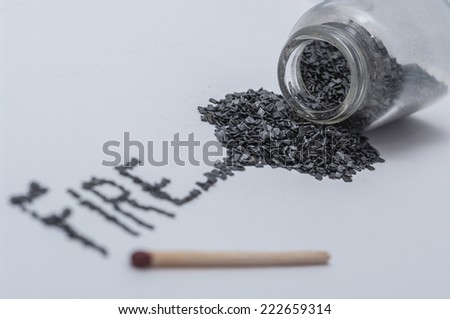 Black gunpowder on white background with word fire written from gun powder and a match stick shallow DOF