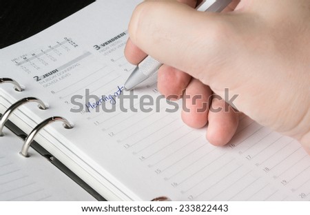 hand writing with silver pen on open business agenda