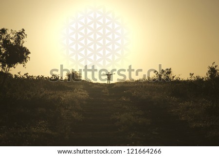 The man standing with his hands up near the setting sun with flower of life