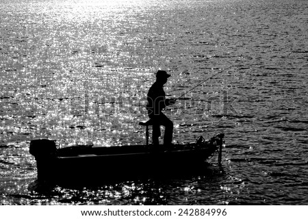 A Silhouette of Fisherman on Fishing boat patiently waiting for the fish to catch a bait in a hot sunny day at noon