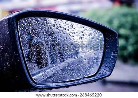 Abstract image of rain drops on car side view mirror and window.