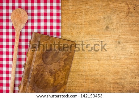 Wooden spoon and book on a wooden board with a checkered tablecloth