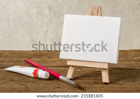 Easel with a blank canvas, paint and brush