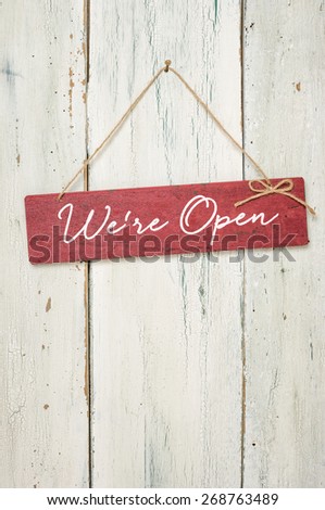 Red sign in front of a white wooden wall - We are open