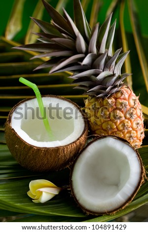 Pineapple, opened coconut and frangipani  flower on a palm leaf