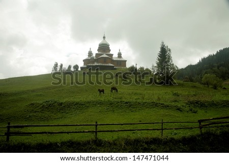 Horses  on a pasture near wooden church on the hill. Ukraine, Carpathian mountains