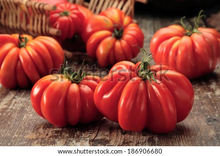 Red beefsteak tomatoes in a basket and on wooden background