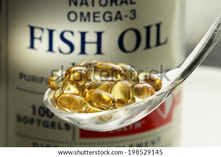 Fish oil softgels in a spoon, bottle with capsules on the background