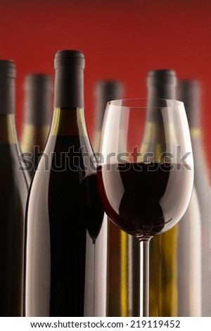 Red wine glass and several bottles of wine  isolated on red  background