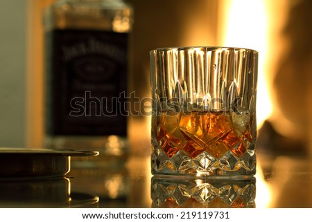 Glass of whiskey and whiskey bottle on the background near the fireplace