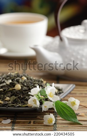 Green tea with jasmine flowers, green tea leaves, tea  cup and tea pot on bamboo table