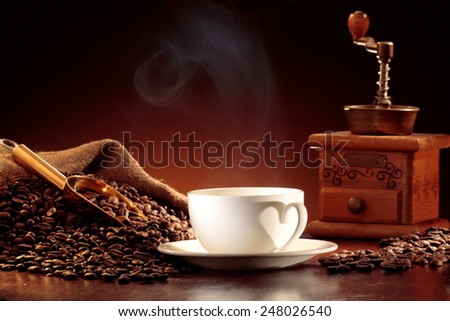 Jute sack of coffee beans with a golden scoop, coffee mill and a steaming cup of coffee