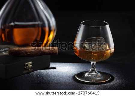 Whiskey glass/ cognac glass, whiskey bottle and cigar on the background
