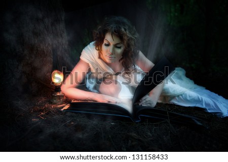 Young fairytale woman reading a magic book in the night,  in the woods