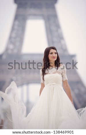 Beautiful delicate bride smiling on her wedding day in Paris with her dress in the air, in front of the Eiffel tour